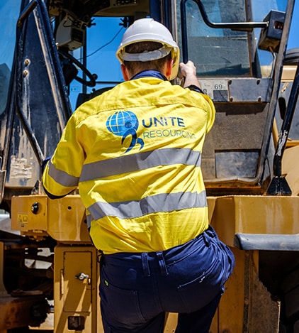 An image of unite resourcing's hired labour worker climbing into a loader wearing hi vis and a safety helmet ppe equipment